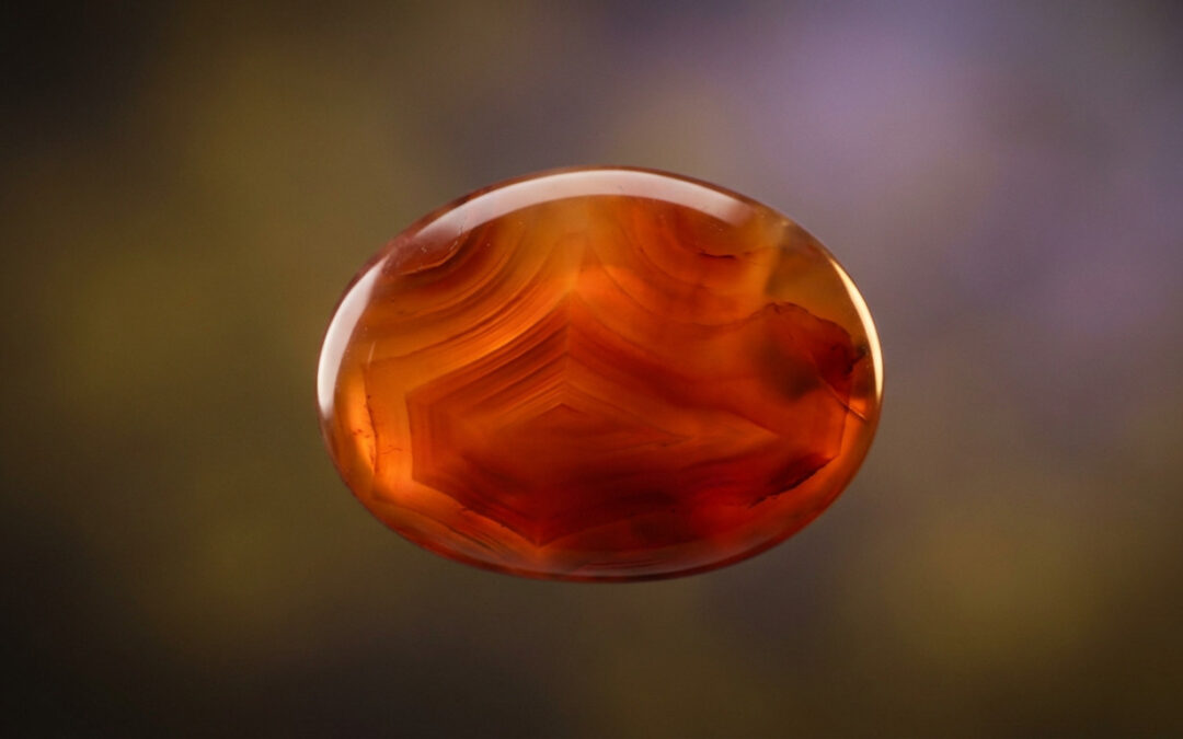 A high-resolution, polished carnelian stone, centered, showing fiery orange and deep red hues, glowing against a soft, blurred background.